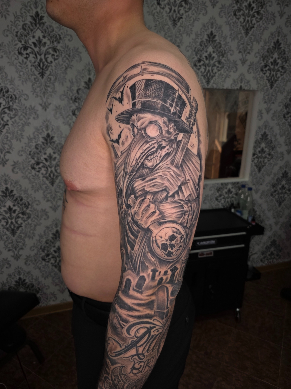 Schwarz-Weiß Tattoo – Skelett mit Rabenmaske und Zylinder, Friedhof-Szene am Arm – Saints Tattoo Pirna, düsterer Realism